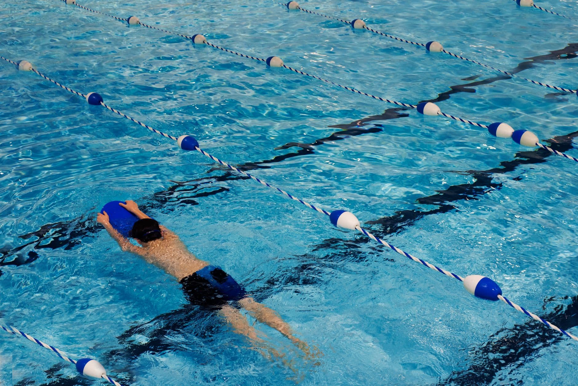 Swimmer kicking with a board held out in front, crossing a sunlit lane pool