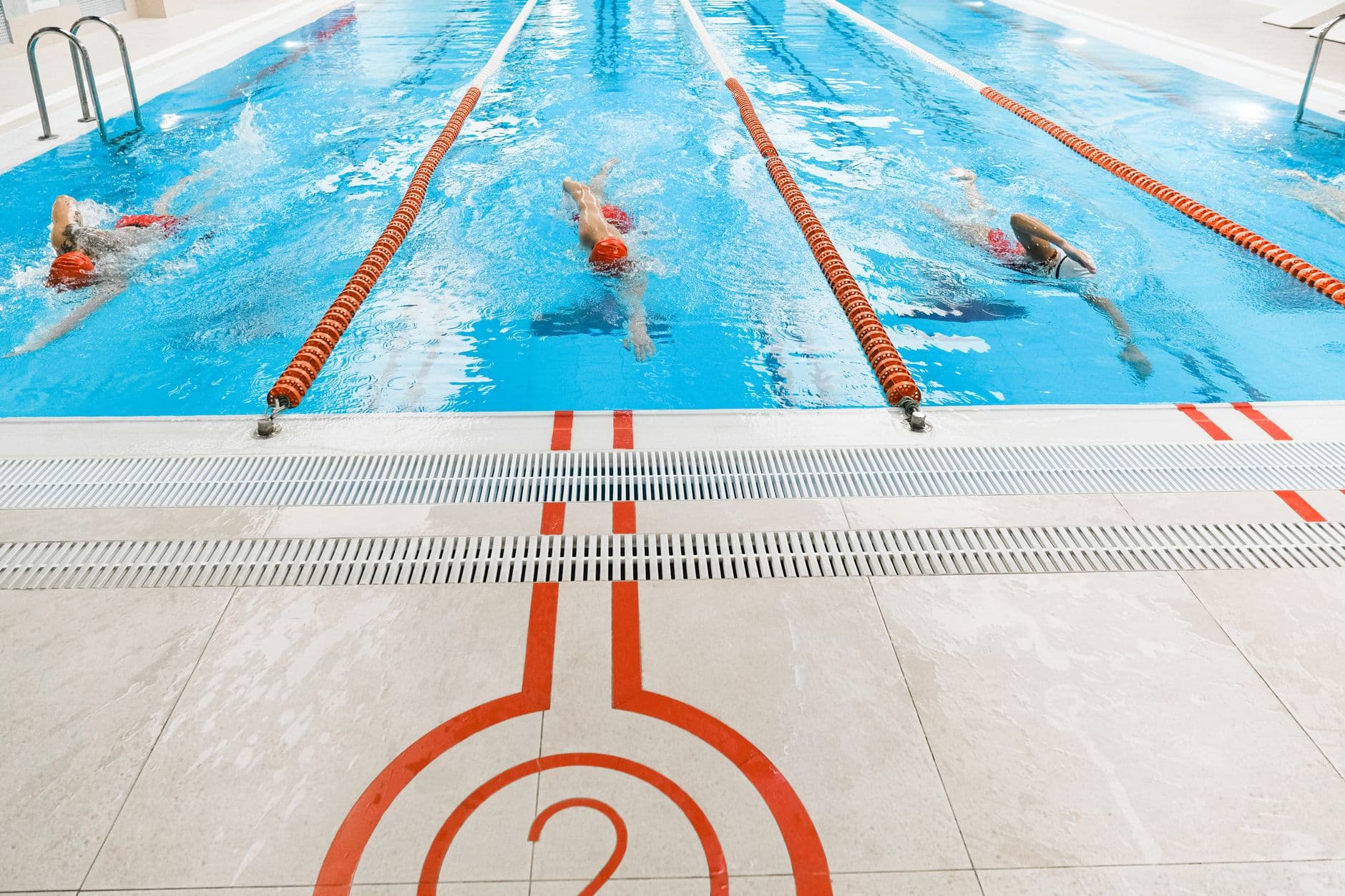 Three swimmers holding a steady freestyle pace in adjacent lanes of an indoor pool