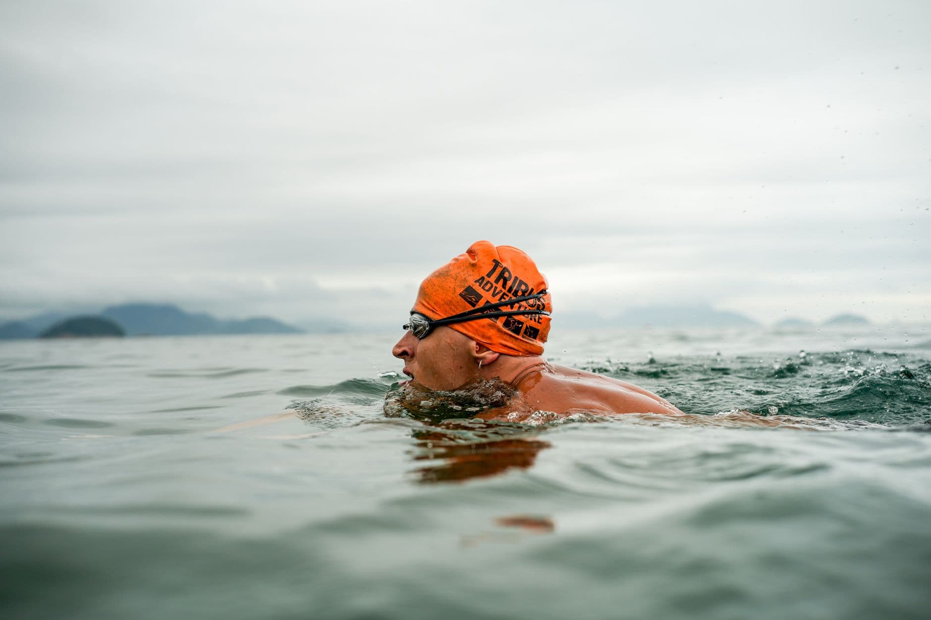 Open-water swimmer in an orange cap sighting forward between strokes