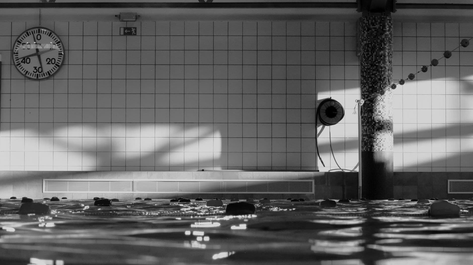 Empty indoor pool photographed in black and white, with the pace clock on the far wall