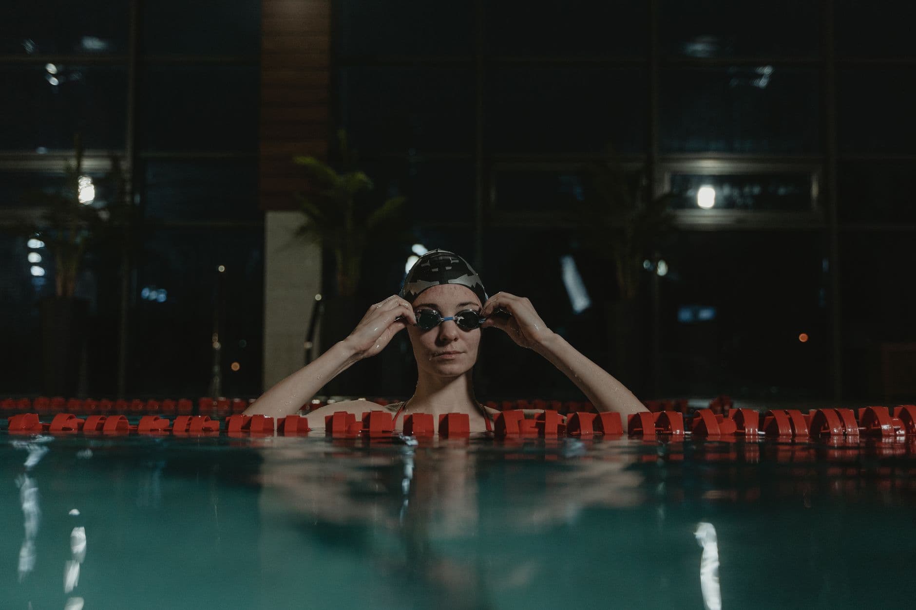 Swimmer adjusting their goggles at the edge of an indoor pool