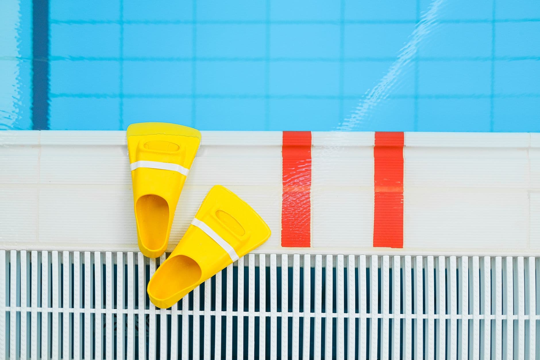 Yellow training fins resting on the tiled edge of a pool