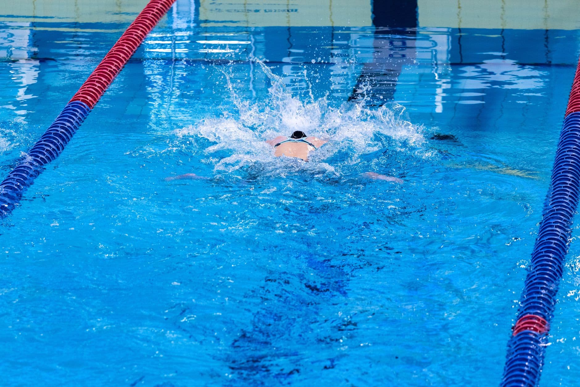 Swimmer on their back mid-backstroke stroke in an indoor pool